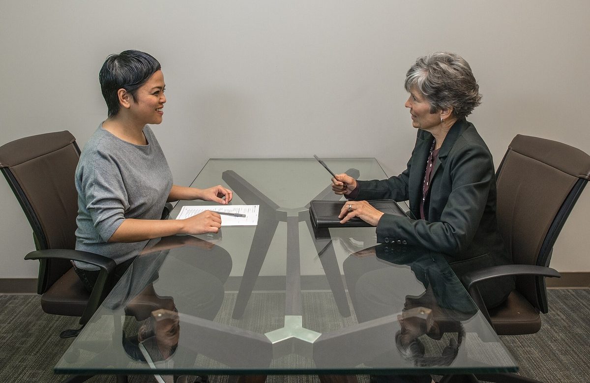 Two colleagues talking across a desk, one taking notes